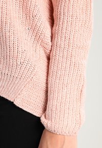 Ljusrosa stickad tröja med en texturerad ribbad mönstring och rullade ärmar. Mjukt material med en avslappnad passform som sträcker sig till ärmarna.