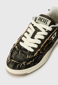 Baskets en denim noir avec des bords effilochés, des lacets blancs et une semelle beige discrète. Présente un patch logo sur la languette et un tissu texturé.