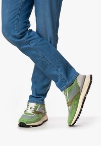 Gröna mockaskor och mesh-sneakers med grå och beige detaljer, med en strukturerad ovandel och en kontrasterande svart gummisula.