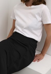 Valkoinen puuvillapaita pyöreällä kaula-aukolla, yhdistettynä korkeavyötäröisiin mustiin hameeseen. Sileä kangas, jossa on hienovarainen rakenne ja saumat.