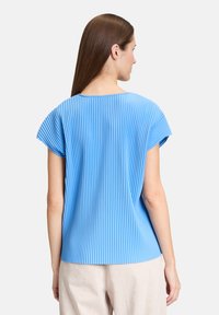 Niebieski plisowany top z krótkimi rękawami, okrągłym dekoltem i gładką teksturą. Widok z tyłu podkreśla plisy sięgające od ramion do hemu.