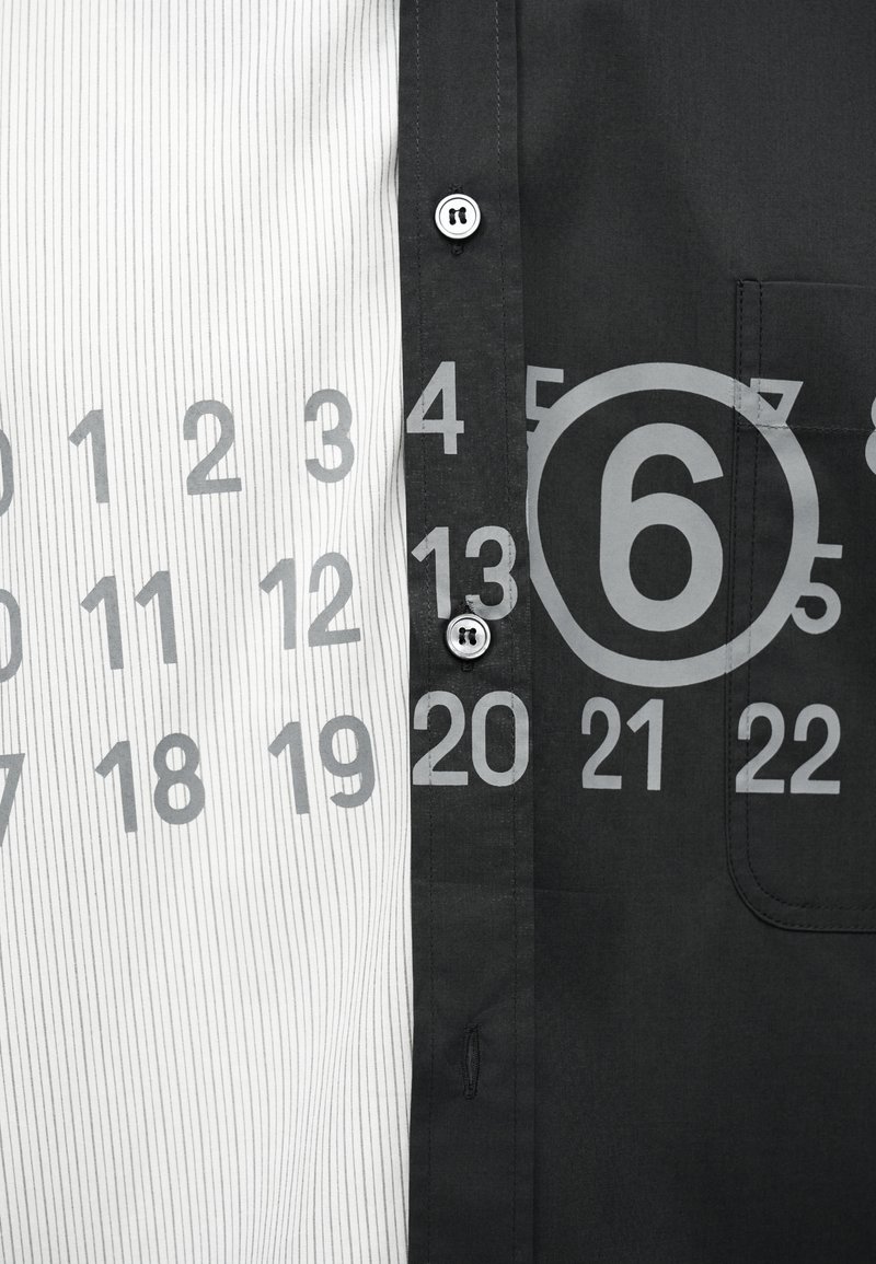 Nahaufnahme eines schwarz-weißen Hemdes mit grauen Kalenderzahlen im Druck, wobei die Zahl 6 auf der schwarzen Seite eingekreist hervorgehoben ist.