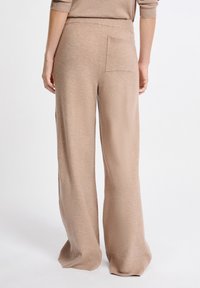 Beige wijde pijpen broek van zacht breimateriaal, met een geribbelde tailleband en een enkele achterzak. Soepele textuur en losse pasvorm.