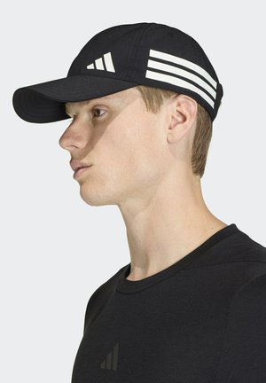 Gorra de béisbol negra con un diseño de tres rayas blancas en el lateral; tiene una visera curvada y una textura suave. Se lleva con una camiseta negra.