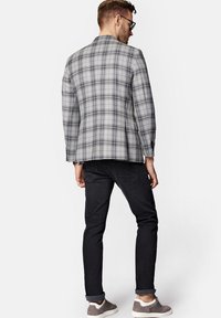 Szary sportowy żakiet w kratkę z czarnymi detalami, zestawiony z czarnymi dżinsami i szarymi sneakersami, widziany z tyłu. Dopasowany krój.