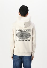 Crème-kleurige hoodie met een grote grafische print op de achterkant, met tekst en een ovale afbeelding. Geribde manchetten en tailleband. Casual pasvorm.