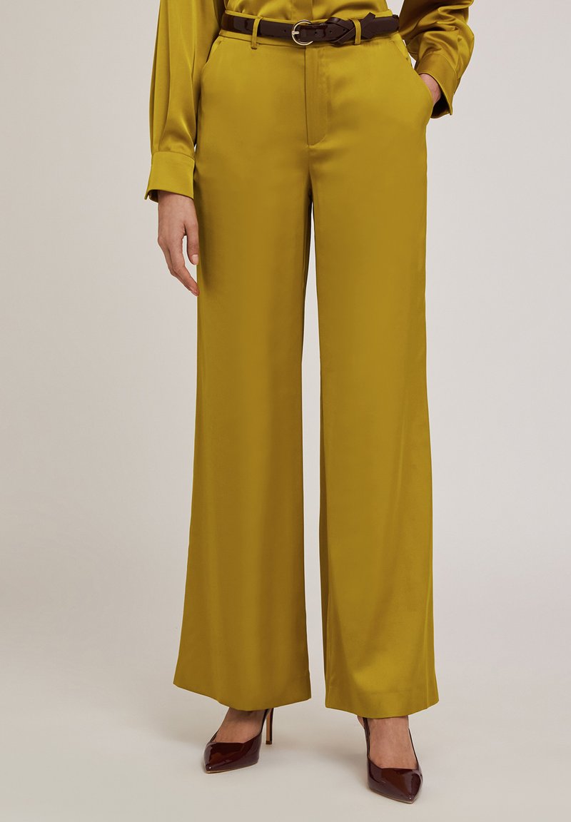 Satin olivgröna vida byxor med sidfickor, ett brunt bälte och slät textur, kombinerat med vinröda högklackade skor.