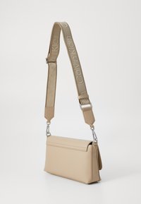 Sac bandoulière beige avec une forme structurée, une texture brillante et une sangle adjustable présentant le logo "Calvin Klein" en broderie claire.