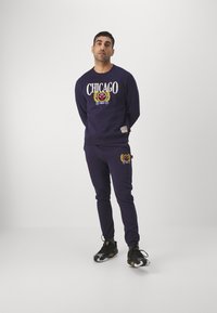 Sudadera navy y joggers a juego con el texto "CHICAGO" y cresta de león bordada. Material de algodón con puños y cinturilla acanalados.