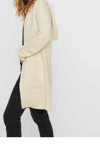 Długi, kremowy kardigan z dzianiny z kapturem, wykonany z fakturowanej tkaniny, z prążkowanymi mankietami i dwoma przednimi kieszeniami.