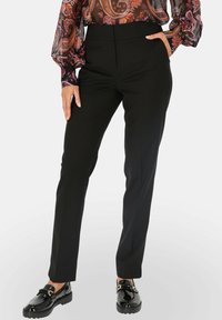 Czarne eleganckie spodnie o wysokim stanie, dopasowane, o gładkiej fakturze, zestawione z błyszczącymi czarnymi butami z ozdobną klamrą.