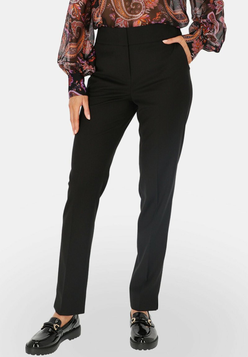 Czarne eleganckie spodnie o wysokim stanie, dopasowane, o gładkiej fakturze, zestawione z błyszczącymi czarnymi butami z ozdobną klamrą.