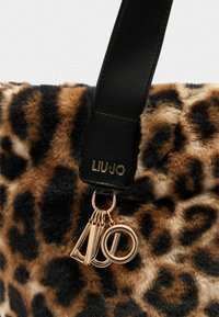 Tote bag van nepbont met luipaardprint, voorzien van een zwarte leren schouderband, met gouden hardware en logo-accenten. Zachte textuur en een opvallend ontwerp.