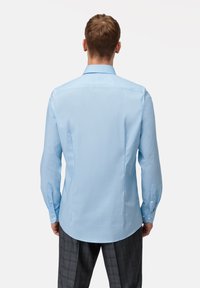 Camicia blu chiaro con bottoni, maniche lunghe, colletto a punta e orlo dritto. Il tessuto appare liscio con una leggera lucentezza.