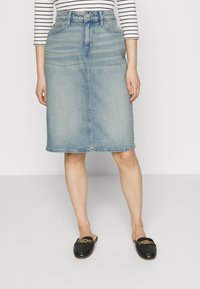 Džínová sukně, světle modrá, ke kolenům, s pěti kapsami, bočními švy a roztrhaným lemem. Spárována s černými mokasíny s zlatým akcentem.