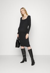 Vestido midi preto, justo, com mangas longas e decote quadrado. Usado com botas pretas de salto bloco até ao joelho e uma mala preta texturizada.