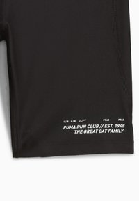 Shorts de compression noirs en tissu lisse et extensible avec des coutures plates. Présente un texte de marque blanc sur la jambe gauche.