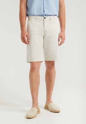 Helle Baumwollshorts mit Knopfverschluss, geradem Schnitt und Seitentaschen. Getragen mit beigen Espadrilles und einem blauen Hemd.