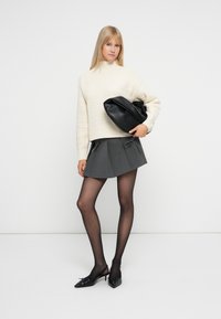 Pull en tricot crème, jupe plissée grise, sac à main noir, collants noirs transparents et talons aiguilles noirs. Design et textures simples et modernes.