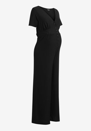 Combinaison de maternité noire à manches courtes, col en V, boutons sur le devant et pantalon à jambes larges sur fond blanc uni.