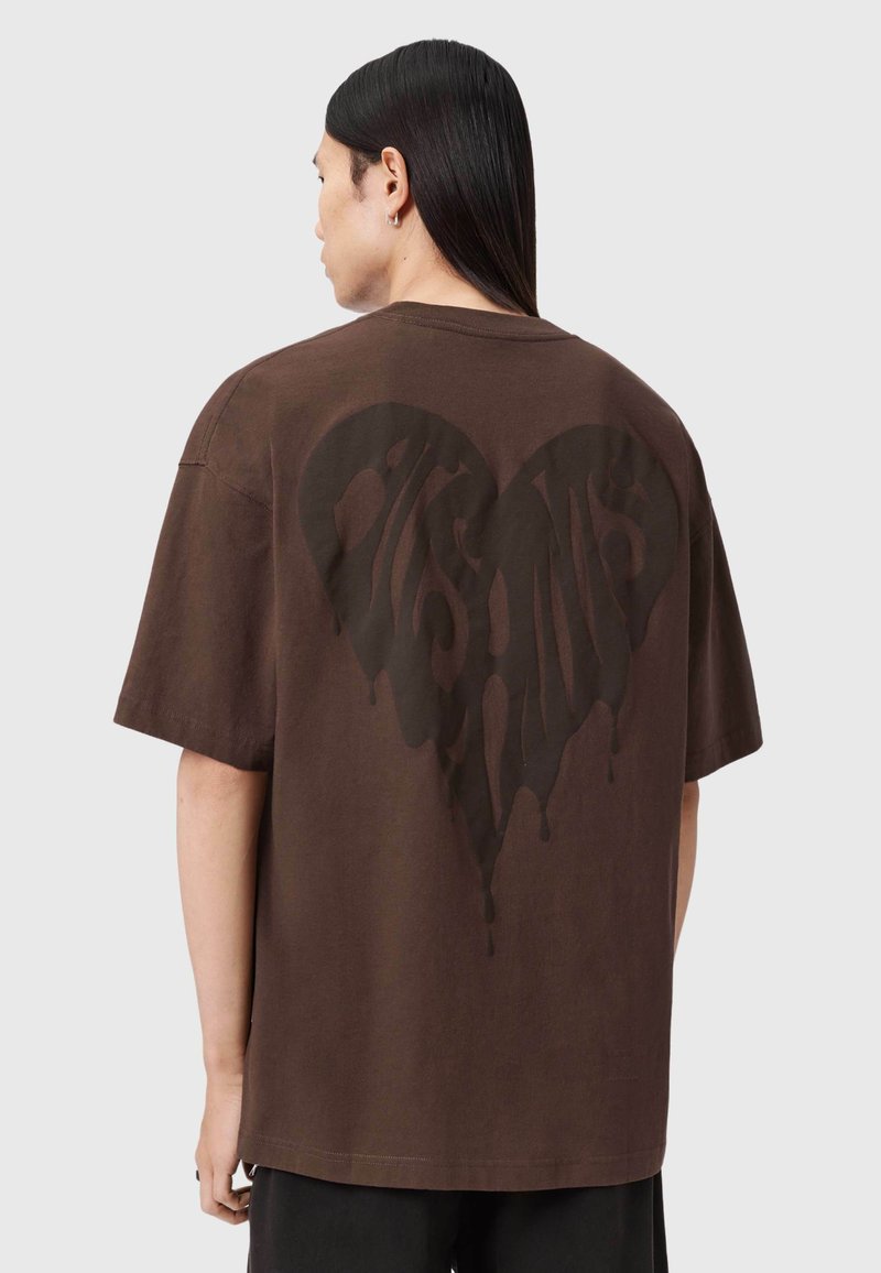 Brun bomulds-t-shirt med stort sort hjertegrafik med drypseffekt på ryggen. Korte ærmer og afslappet pasform.