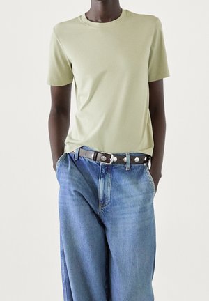 Light green cotton t-shirt with a round neck, paired with high-waisted blue denim jeans and a brown leather belt with silver hardware.
