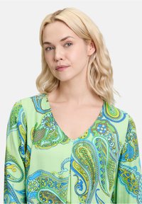 Multicolor blouse met een groene achtergrond en blauwe en gele paisleypatronen, V-hals en lange mouwen. Soepele stoftextuur.