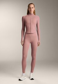 Fitted athletic set in soft pink fabric; features a full-zip long-sleeve top with ribbed accents and high-waisted leggings.