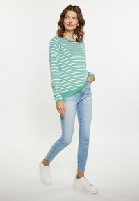 Pulover verde cu dungi albe, cu un guler rotund, asortat cu blugi skinny albaștri deschiși. Tenis albi completează ținuta.