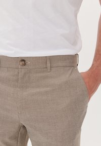 Beige, gestructureerde broek met een rechte pasvorm. Beschikt over een enkele knoop, riemlussen en zijzakken, gedragen met een plain wit t-shirt.
