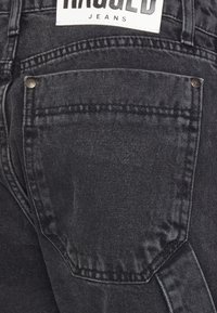 Černé džíny z denimu s tmavým omakem. Mezi jejich vlastnosti patří zadní kapsa se stehmi a visačka s nápisem "Rugged Jeans."
