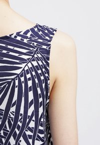 Hedvábná bezramínková blůza s námorně modrým a bílým tropickým vzorem listů, hladkým materiálem a uvolněným střihem, který zdůrazňuje čistý výstřih.