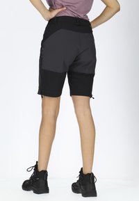 Svarta och grå utomhusshorts med hög midja, fickor med dragkedja, en åtsittande design och textilerat tyg, kombinerat med svarta ankelstövlar.