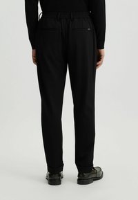Schwarze Hose mit lässigem Schnitt, mit einem elastischen Bund, zwei hinteren Taschen und einem glatten, texturierten Stoff.