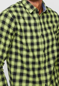 Grünes und schwarzes Karohemd mit Button-down-Kragen, aus einem strukturierten Stoff und mit kontrastierenden Denim-Akzenten am Kragen.