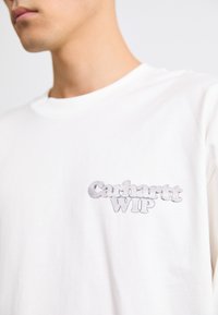 Bijela pamučna majica sivo stiliziranim "Carhartt WIP" logotipom na lijevoj strani grudi. Jednostavan dizajn s okruglim izrezom.