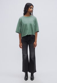 Sweat-shirt vert court à manches larges, associé à un jean noir délavé évasé et des bottines noires pointues. Texture de tissu lisse.