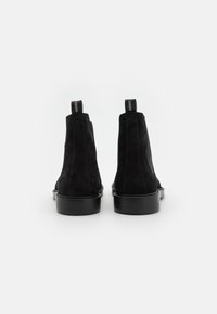 Bottines en daim noir avec un bout lisse, semelle en caoutchouc noir robuste et languettes de marque à l'arrière. Design minimaliste avec une silhouette élégante.