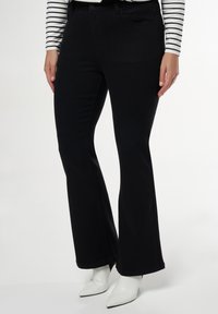 Zwarte flared jeans van denim, met een klassieke vijf-pocketontwerp en een gladde textuur, gecombineerd met witte pointy-toe laarzen.