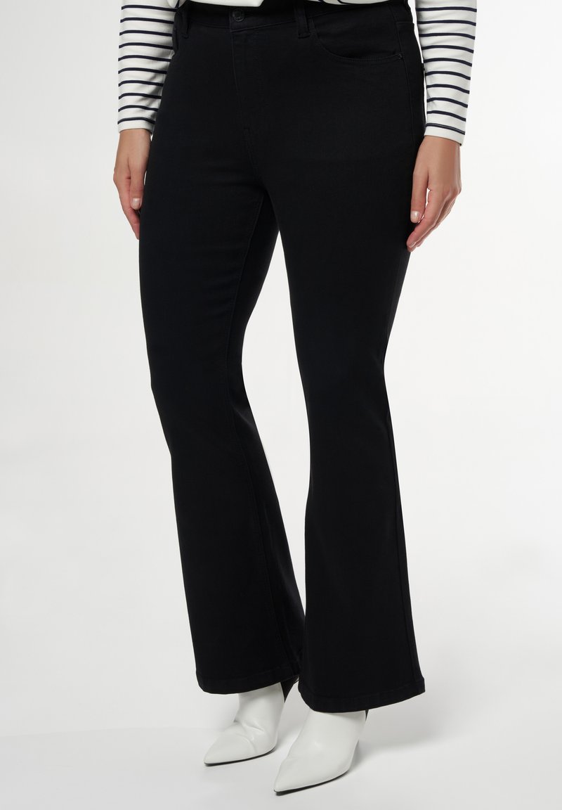 Zwarte flared jeans van denim, met een klassieke vijf-pocketontwerp en een gladde textuur, gecombineerd met witte pointy-toe laarzen.