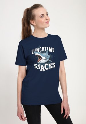 Navy blue t-shirt featuring a shark graphic with open jaws, surrounded by the text "LUNCHTIME SNACKS" in bold white letters.