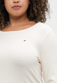 Krämfärgad långärmad topp i ribbat material. Har en bred halsringning och en liten broderad logotyp på bröstet.