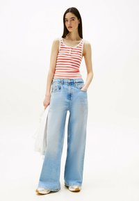 Top sin mangas a rayas en rojo y blanco, combinado con unos vaqueros de pierna ancha en azul claro. Los vaqueros tienen una cintura alta y un corte holgado con bolsillos.