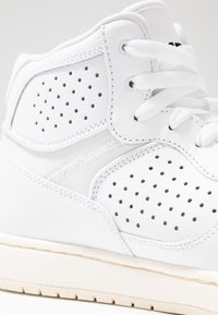 Sneaker alta bianca con pannelli perforati, tomaia in pelle liscia, lacci tondi e suola in gomma color crema. Accenti cuciti visibili.