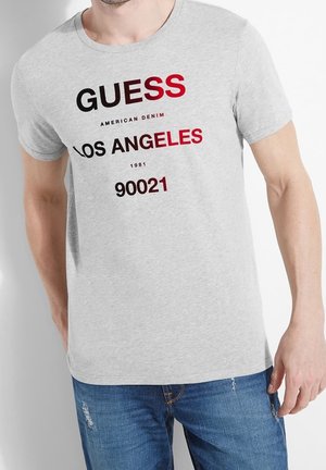 Jasnoszary t-shirt z krótkim rękawem z wyraźnym czarnym i czerwonym napisem „GUESS LOS ANGELES 1981 90021”, wykonany z miękkiej bawełny.
