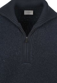 Donkerblauw gebreide trui met een geribde halve ritskraag en metalen ritstrekkertje, met het "Suitable" merklabel zichtbaar aan de binnenkant van de kraag.