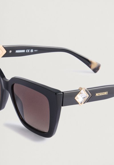 Črne pravokotne sončna očala s rjavim prelivom leč, zlatimi kovinskimi detajli in okrasjem v obliki diamanta. Ime blagovne znamke "Missoni" vidno.