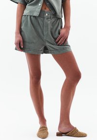 Lichtgroene katoenen shorts met een relaxte pasvorm, voorzien van voorzakken en een elastische taille. Gecombineerd met beige geweven instap schoenen.