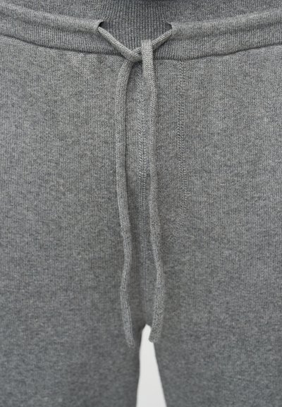 Κοντινή λήψη γκρι πλεκτού παντελονιού με δέσιμο κορδονιού στη μέση, που δείχνει την υφή του υφάσματος και τις λεπτομέρειες της ραφής.