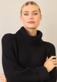 Maglione a collo alto nero a coste, con una texture grossa, caratterizzato da un colletto alto e una vestibilità rilassata, che presenta un design in maglia spessa.